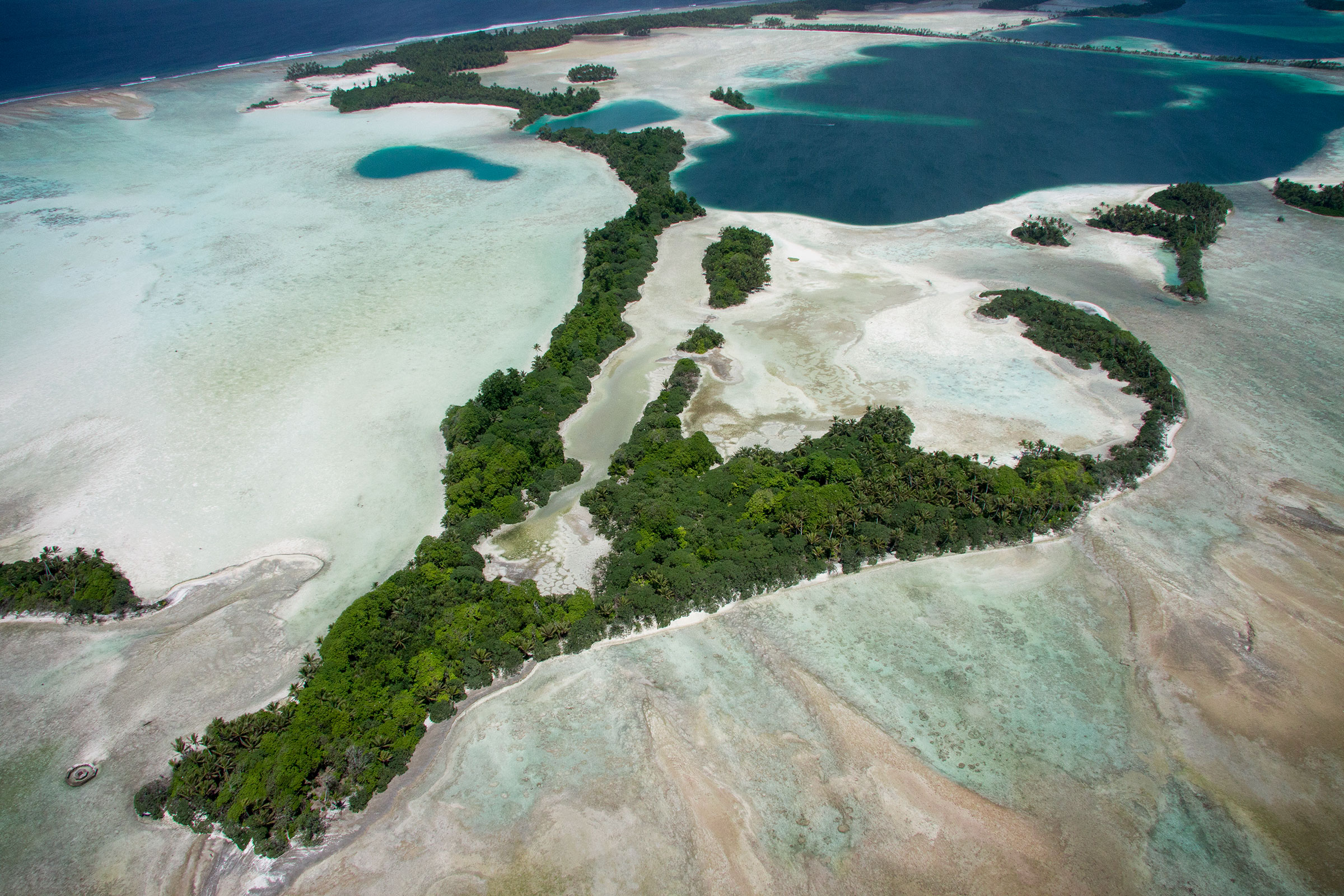 A lush green island surrounded by sand and deep blue water seen from above.